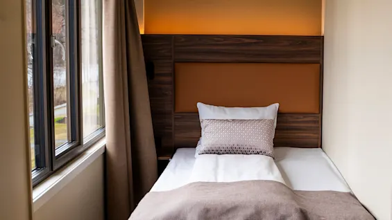 A cozy hotel room with a single bed, warm lighting, and a window offering a view outside.