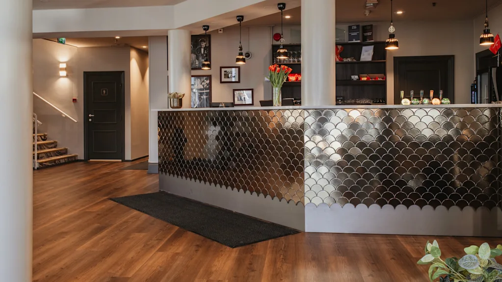 Et moderne hotelreceptionsområde med en stilfuld, metalflisebelagt disk, trægulve og en trappe.