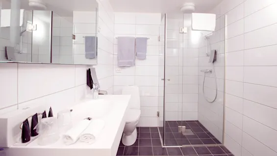 Ett modernt badrum med glasduschvägg, vita kaklade väggar, en dubbelhandfat och en toalett.