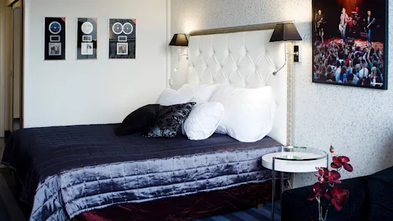 A neatly made bed with decorative pillows against a tufted headboard, flanked by music-themed wall decor, in a cozy, modern room.