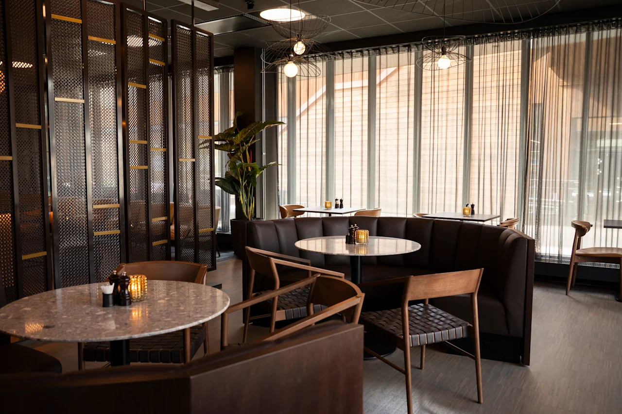 Et stilig restaurantinteriør med marmorbord, brune skinnseter og store vinduer med tynne gardiner.