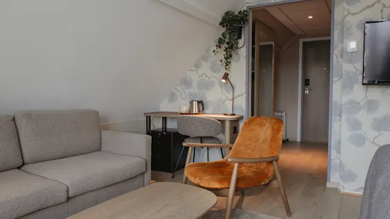 Et hyggeligt hotelværelse med en komfortabel sofa, en lænestol og et funktionelt arbejdsområde med skrivebord og lampe.