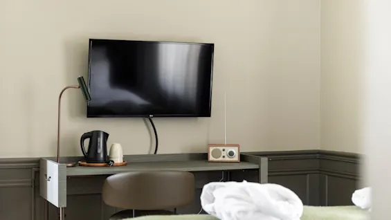 Viihtyisä hotellihuoneen työpöytäalue, jossa on televisio, vedenkeitin ja radio, valmiina rentouttavaan oleskeluun.