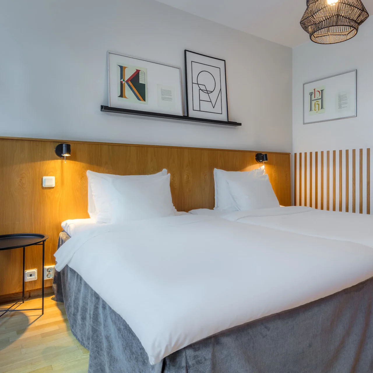 Two white beds in a tidy bedroom, with artwork above and a wooden headboard.