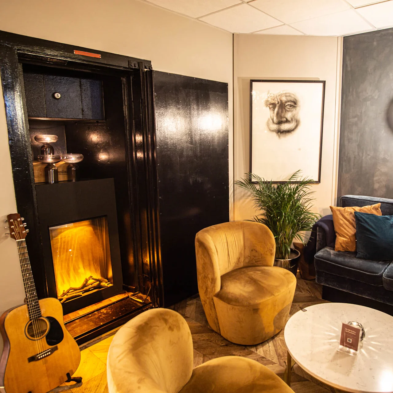 A cozy corner with a velvet sofa, armchairs, an artificial fireplace, and decorative lighting in a warmly lit room.