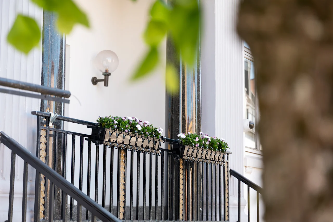 An elegant outdoor stairway with floral decorations and a vintage-style lamp on a white building facade.