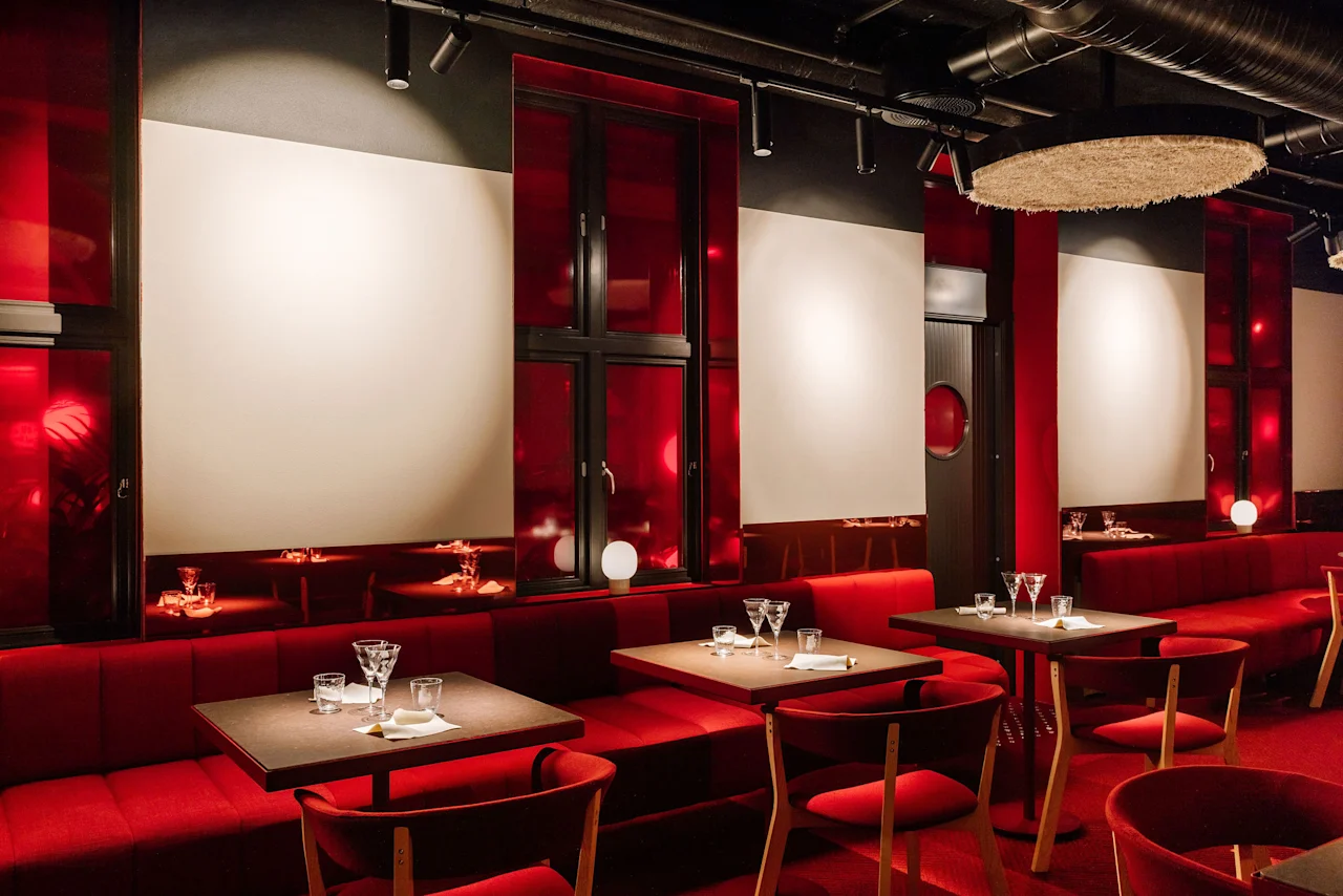 A stylish restaurant interior with plush red booth seating, matching chairs, and dark wooden tables set for dining.