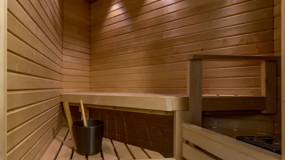 Wooden sauna interior with benches, a bucket, and a ladle, in a warmly lit, relaxing space.