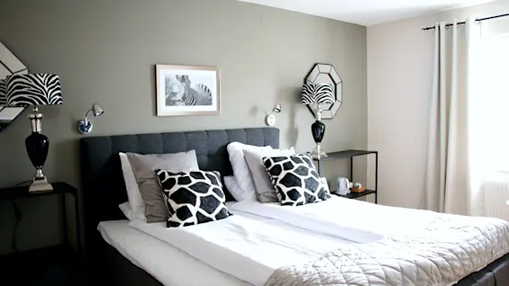 Modern hotel room featuring a made double bed, zebra-patterned lamps and pillows, and stylish decor.