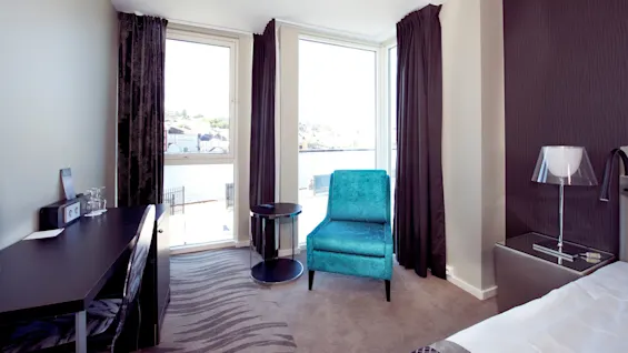 A hotel room with modern furniture overlooking a waterside view through large windows, giving a feeling of comfort and elegance.