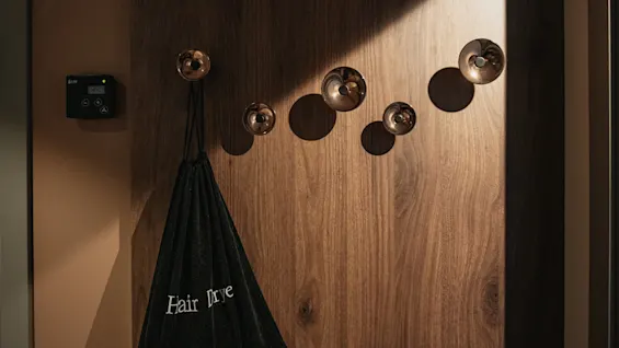 En hårfønerpose henger på en stilig trevegg med dekorative kroker, noe som antyder et velutstyrt hotellrom.