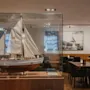 En detaljeret modelsejlbåd i en glasvitrine, med et restaurant- eller loungeområde synligt i baggrunden. Tekst på båden: RORO WILH R LUNDGREN.