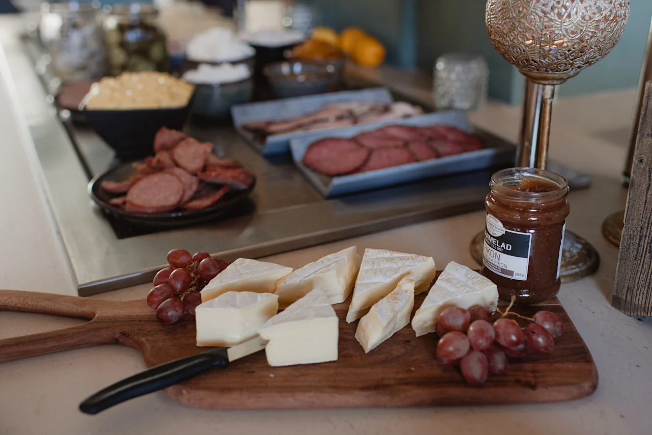 En matutställning med ost, vindruvor, sylt märkt SYLT MELAD FIKON och skivat kött på ett serveringsbord.