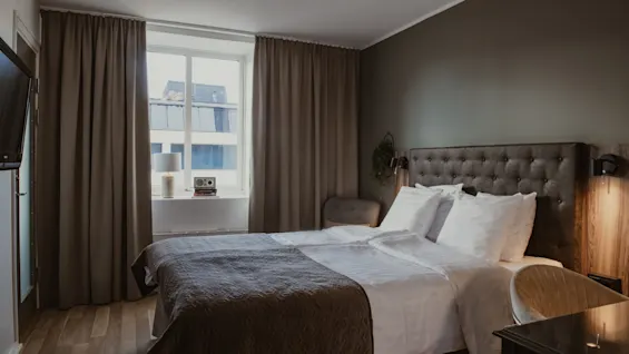 Viihtyisä hotellihuone, jossa on mukava sänky, ikkuna kaupunkinäköalalla ja lämmin valaistus rentouttavaan oleskeluun.
