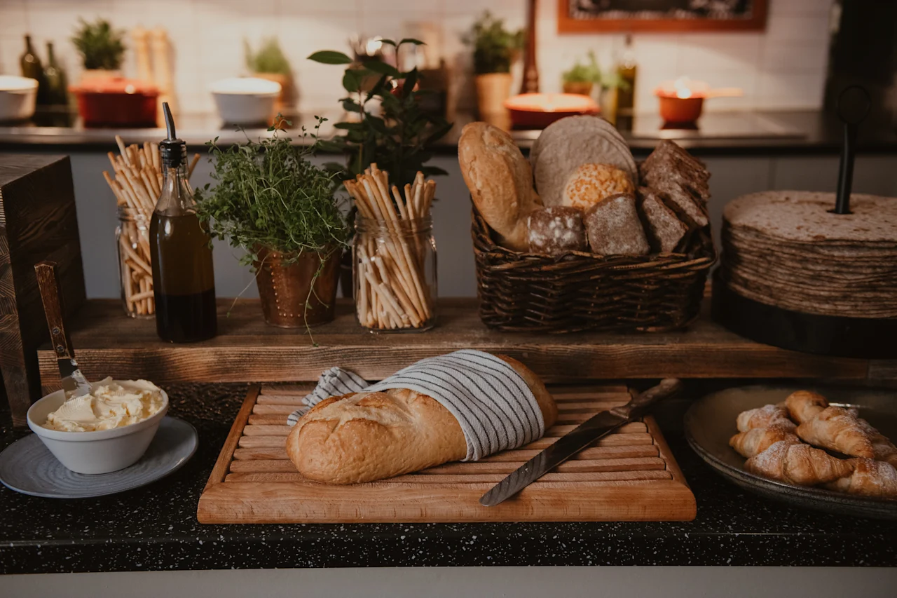 A rustic bread station with fresh loaves, pastries, butter, olive oil, and herbs, ready for a delicious meal.