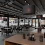 Interiør av en moderne restaurant med tomme flettede stoler og bord under et baldakintak. Hengende lys gir atmosfære, store vinduer gir utsikt over gaten utenfor.