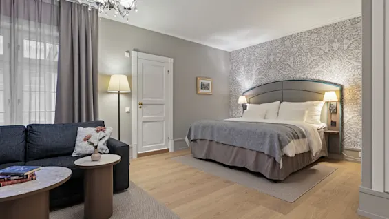 Et hyggeligt hotelværelse med en stor seng, en komfortabel sofa og elegant indretning, perfekt til afslapning.