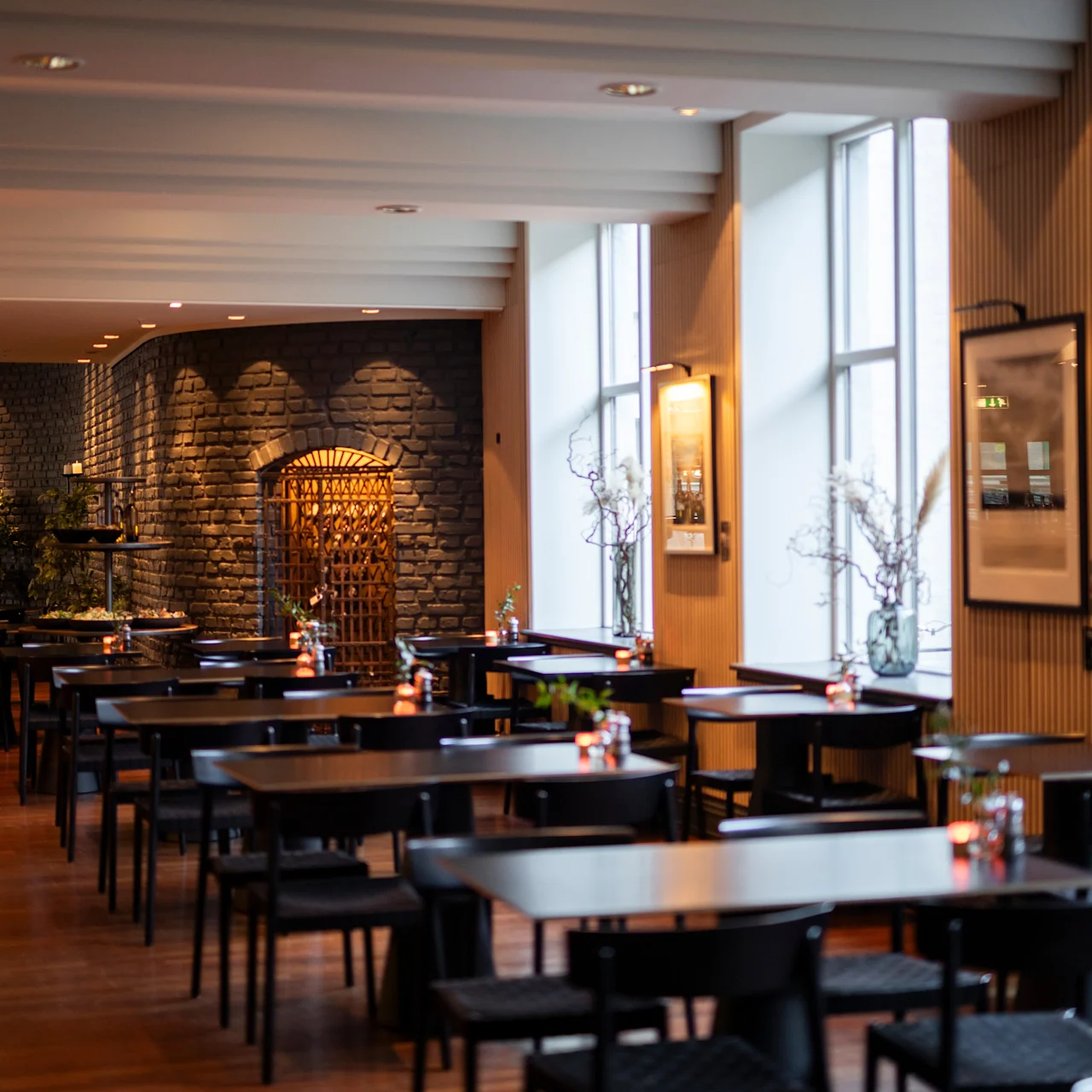 Borde og stole er pænt arrangeret i en rummelig, velbelyst restaurant med store vinduer og murstensvægge. Atmosfæren er hyggelig og indbydende med moderne indretning og subtil belysning.
