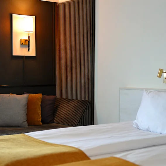 Mysigt hotellrum med en nybäddad säng i förgrunden och en varm sittgrupp i bakgrunden