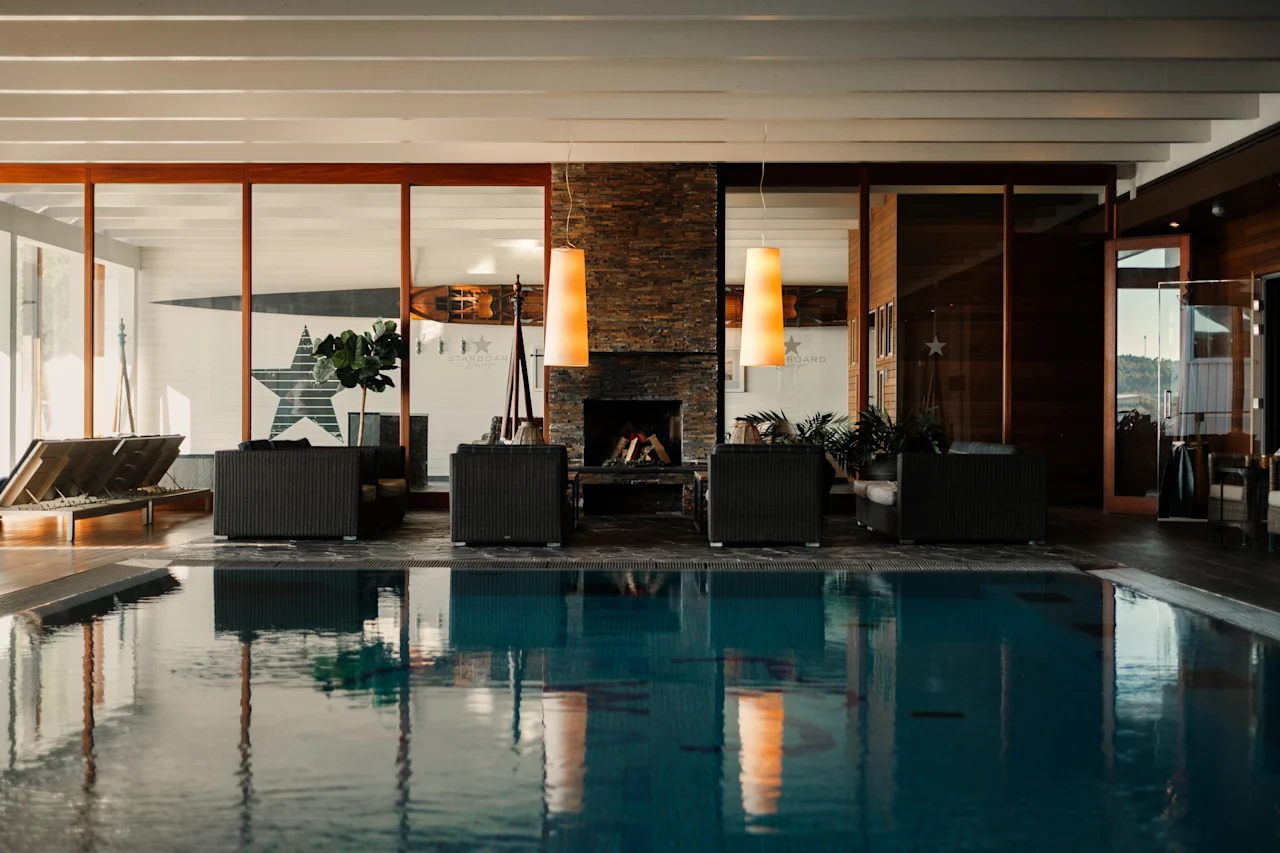 Et luksuriøst indendørs poolområde med en hyggelig lounge, pejs og store vinduer, der tilbyder en afslappende atmosfære.