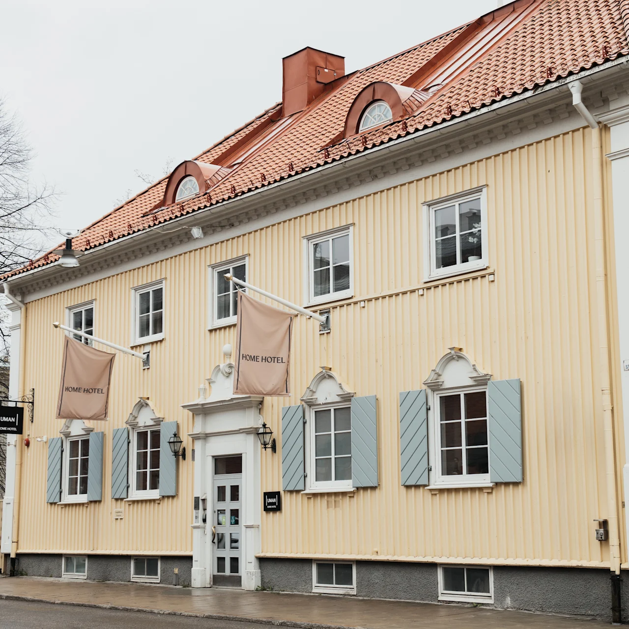 A two-story yellow building with a red-tiled roof features signs reading "RUM," "RUM HOTEL," and "POMP UPPSALA." It is situated along a quiet street with bare trees.