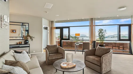 En moderne stue på Quality Hotel Ulstein med sofa, lenestoler og et skrivebord, med panoramautsikt over sjøen og fjellene.