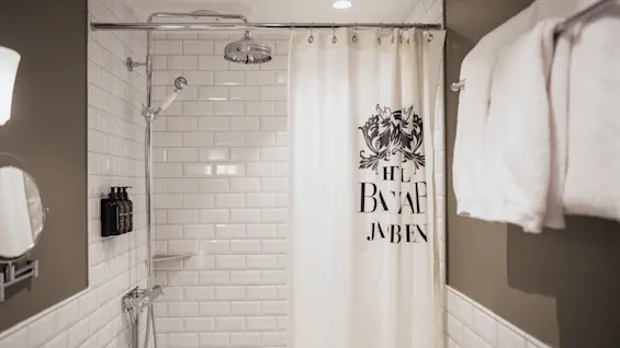 Home Hotel Baltzar - Standard Twin. A clean shower with white subway tiles, a shower curtain with HTL BALTZAR JABEN text, and fresh towels.