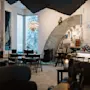 Et hyggeligt rum med moderne møbler og dekorativ belysning. Et vindue viser snedækkede træer udenfor. Tekst på væggen inkluderer: "ICEHOTEL built in 1989," "600 tons of ice," "12 weeks to build."