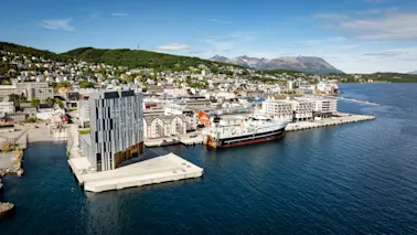 Quality Hotel Harstad, en moderne bygning på en brygge i en livlig byhavn med et stort skip fortøyd, omgitt av åser og fjell.