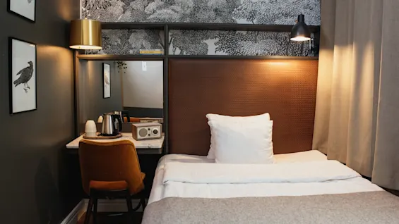 Et indbydende hotelværelse med en pænt redt seng, et praktisk skrivebordsområde med en elkedel og et stilfuldt tapet med naturtema.