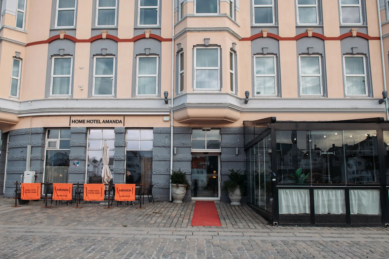En charmerende bygning med skiltet HOME HOTEL. Rød løber til indgangen, med udendørs siddepladser og et indglasset område.