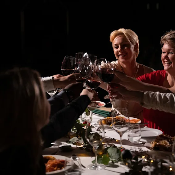En gruppe mennesker som skåler med glassene sine rundt et hyggelig middagsbord i dempet belysning