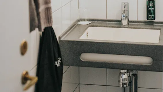 A bathroom sink with towels on the wall and reflections visible in a mirror, indicating a tidy space.