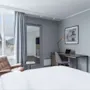 Lyst og moderne hotellrom med skrivebordsplass, lenestol ved vinduet og en behagelig seng.