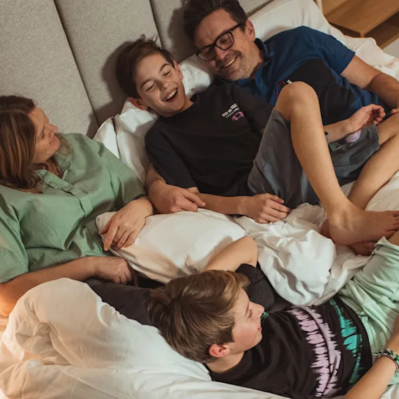 En familie på fire ligger sammen i en romslig hotellseng, smiler og ler under oppholdet sitt.