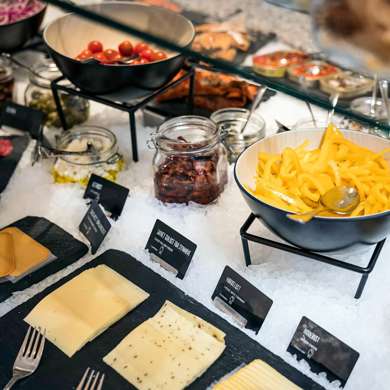 En val av delikatessvaror på is inkluderar skivade köttbitar, ostar, paprikor, tomater och burkar med oliver. 
