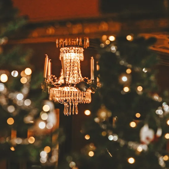 A glowing crystal chandelier hanging in a cozy, festive room decorated with warm Christmas lights.
