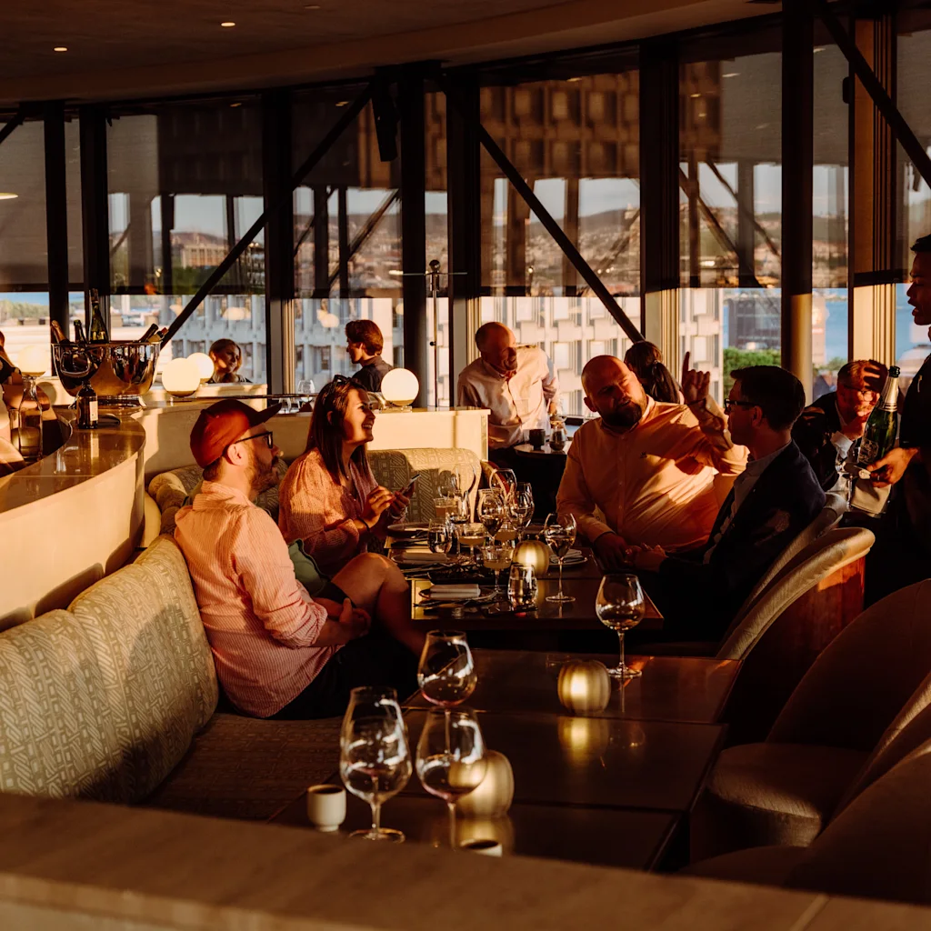 People enjoying drinks and conversation in a stylish bar with city views at sunset.