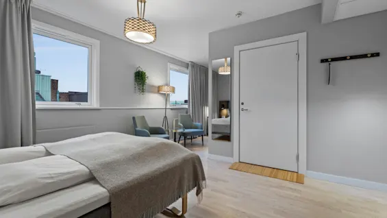 Ett ljust och modernt hotellrum med en bekväm säng, en mysig sittgrupp och stora fönster med utsikt.