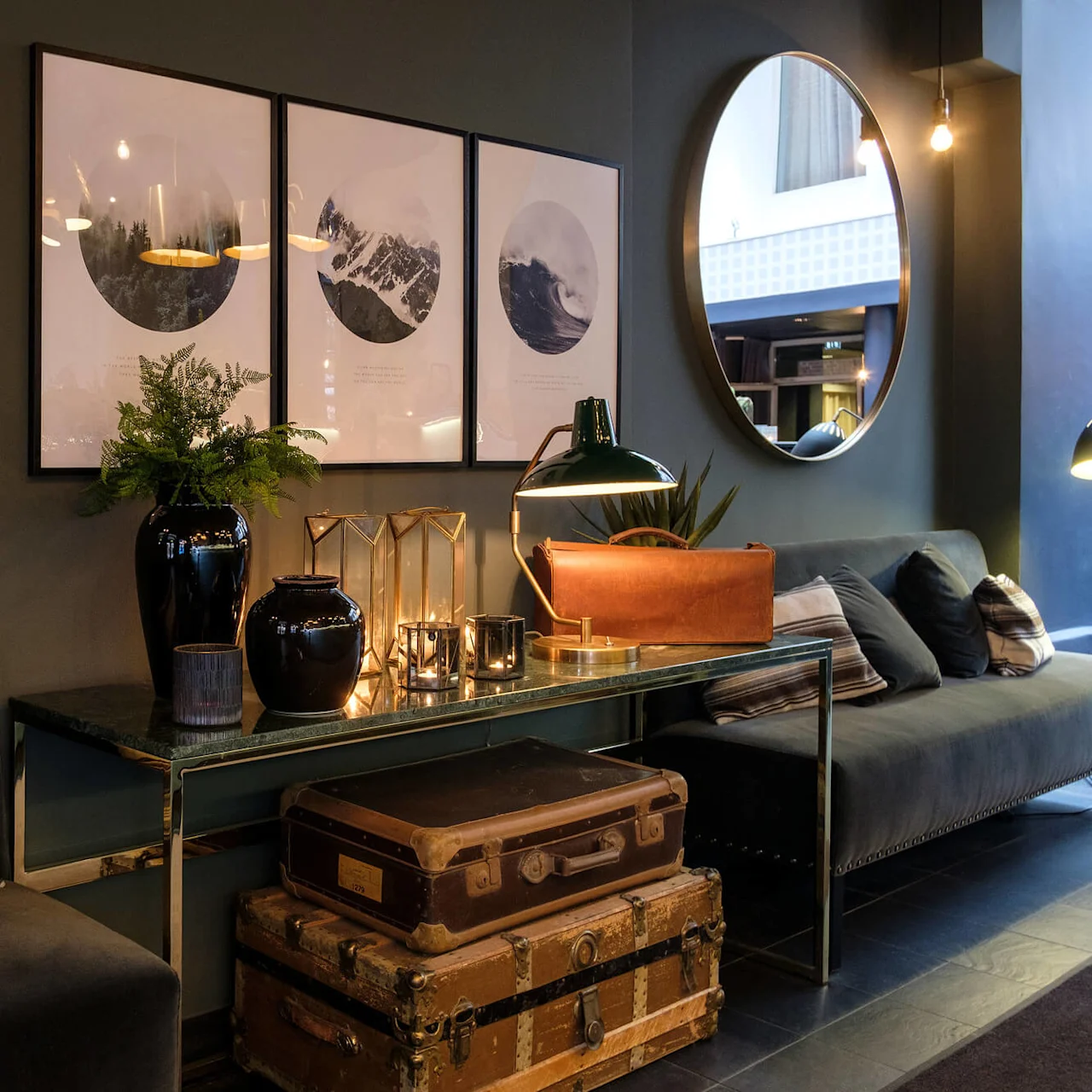 Velvet sofa with pillows, decorative items on tables, framed pictures on wall, large mirror reflects interior of an elegant lounge.