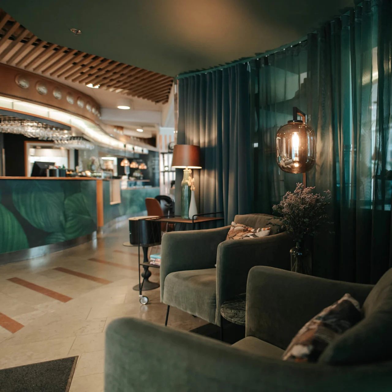 Comfortable armchairs are arranged for relaxation in a dimly lit lounge area with curtains, subdued lighting, and a counter in the background.