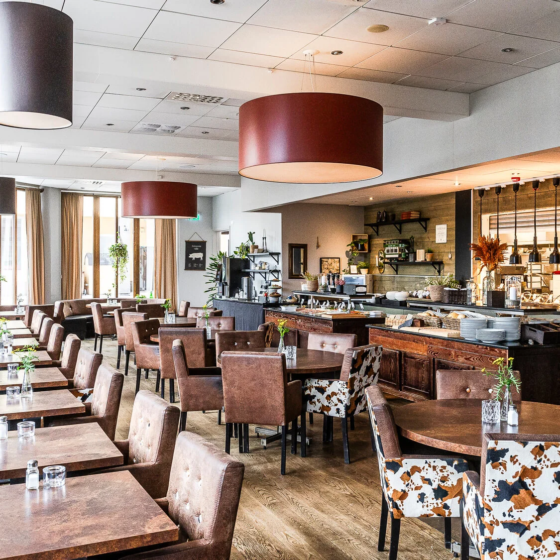 En restauranginteriör med tomma bord, stolar och en bufféuppsättning, som visar en rustik och mysig atmosfär.