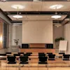 A modern conference room with rows of tables and chairs facing a large projection screen, ready for a presentation.