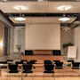A modern conference room with rows of tables and chairs facing a large projection screen, ready for a presentation.