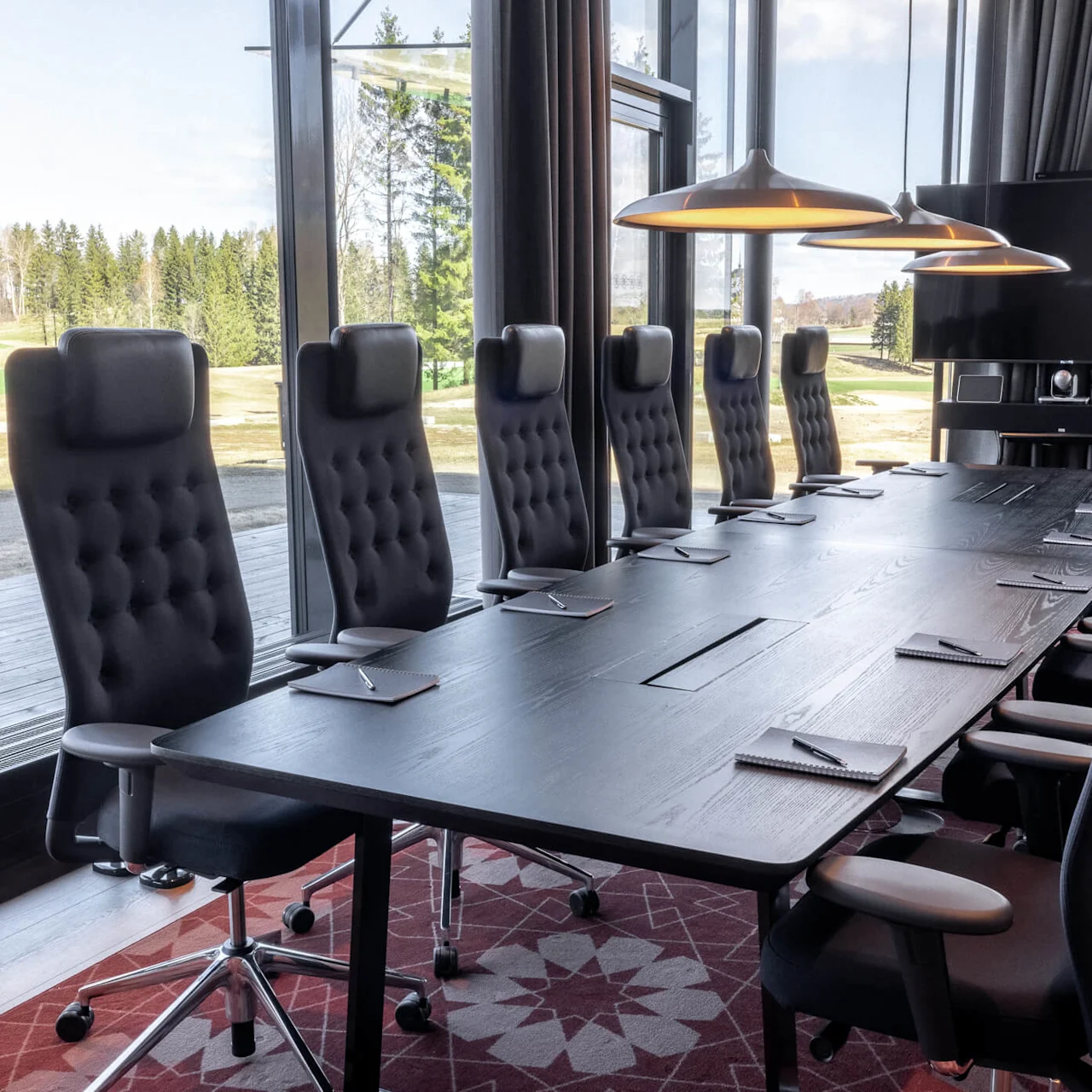 Ett modernt konferensrum med ett långt bord, stolar med hög rygg och utsikt över en golfbana genom fönster från golv till tak.
