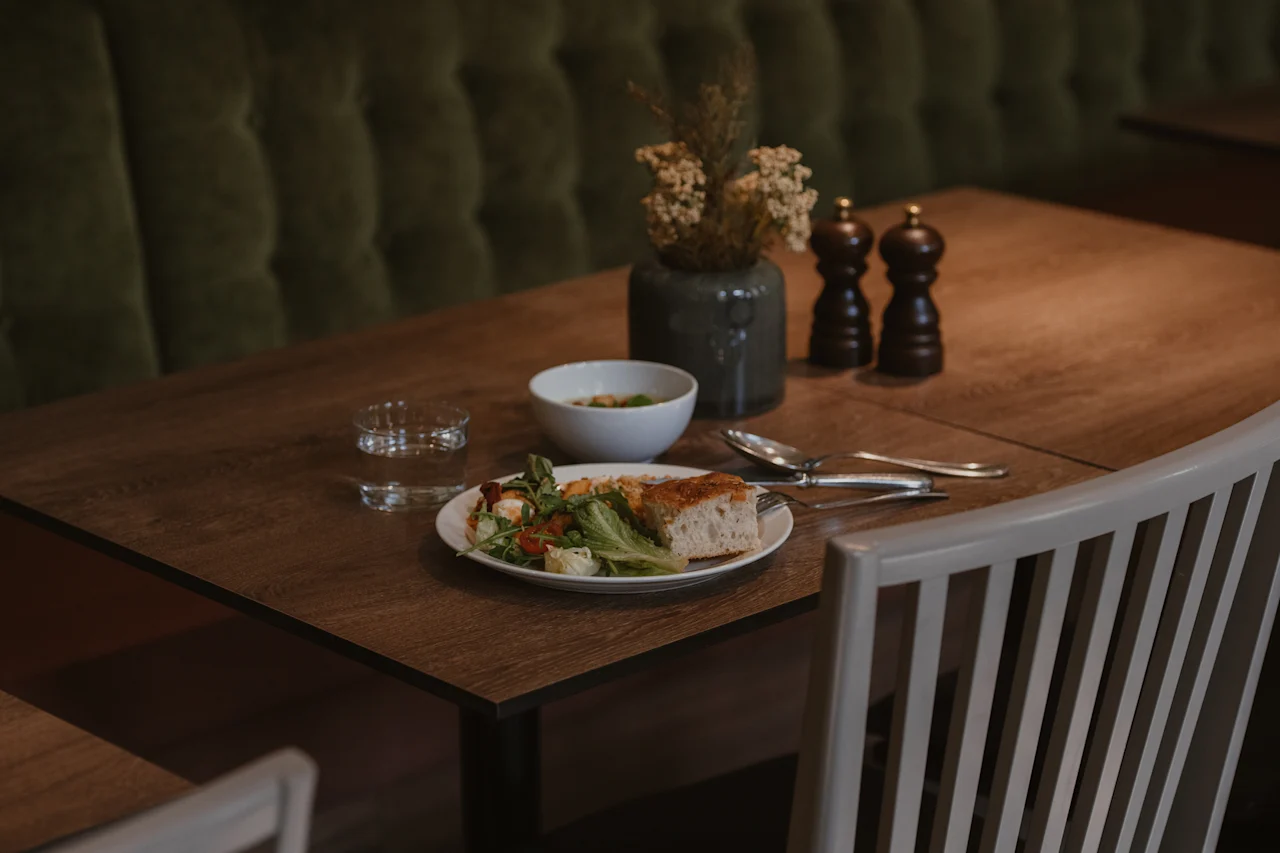 Et bord dekket for et måltid med en frisk salat, brød, vann og krydder i en koselig restaurantsetting.
