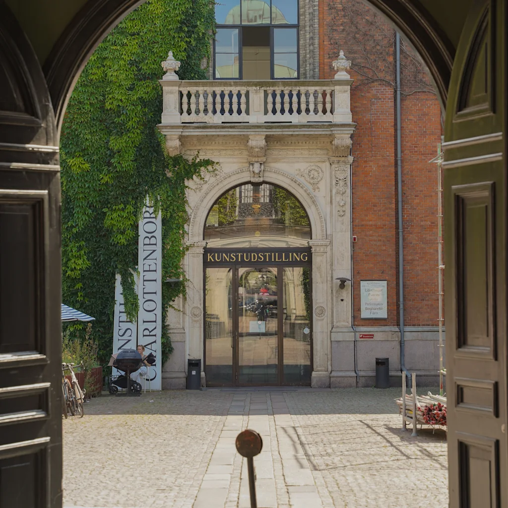 View through an archway to Kunsthal Charlottenborg in Copenhagen, an art exhibition entrance. KUNSTUDSTILLING. People entering.