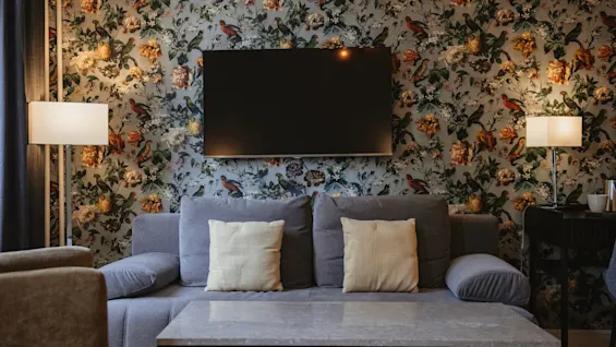 Et hyggeligt opholdsområde på Home Hotel Norre Park i Halmstad med en sofa, sofabord og et TV på en blomstret tapetseret væg.