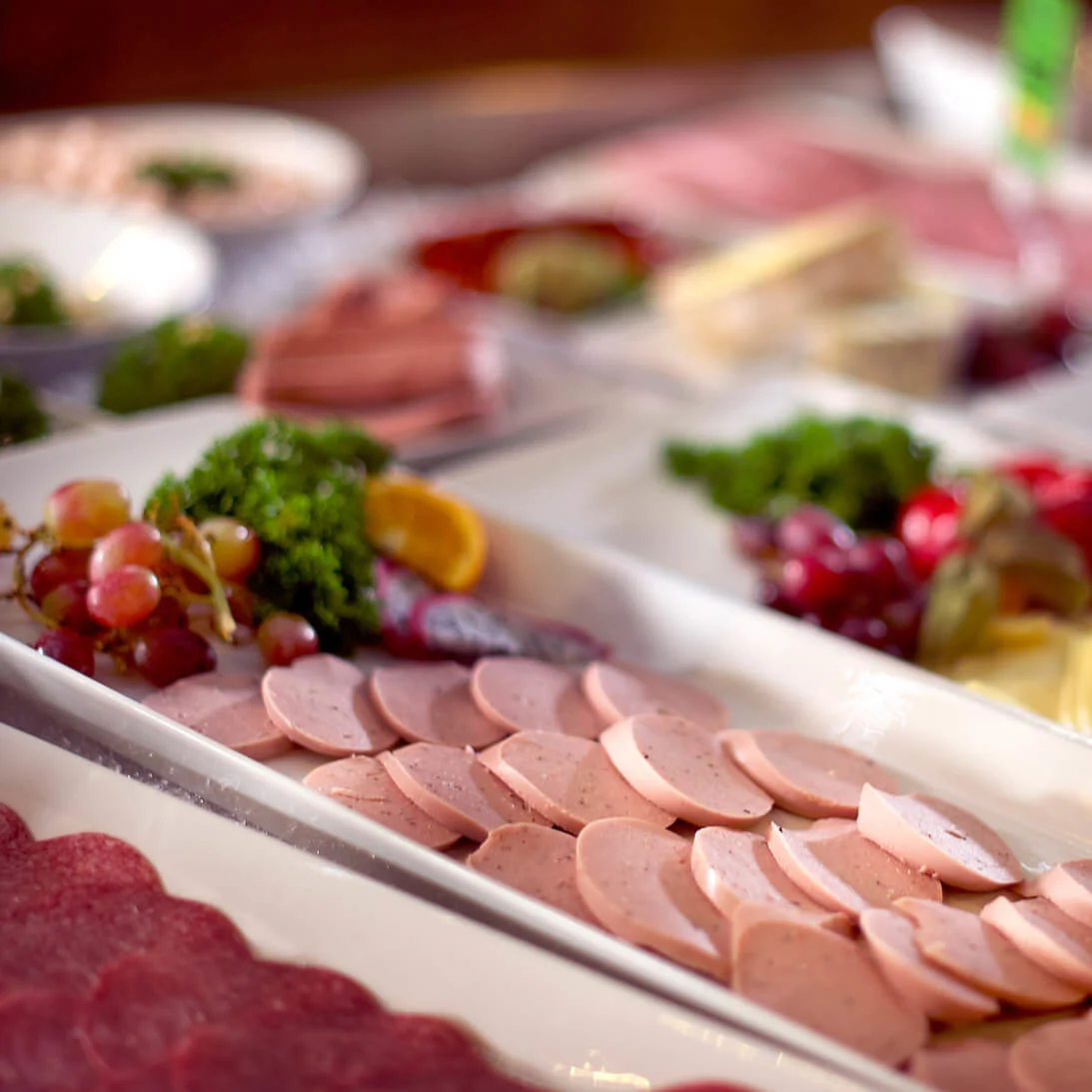 En buffé med blandade kallskurna och ost, snyggt arrangerade på vita fat, antyder en catering- eller gästfrihetskänsla.