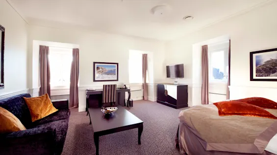 Ett välbelyst hotellrum med elegant möblering, en plyschsoffa och en prydligt bäddad säng i en bekväm och inbjudande atmosfär.